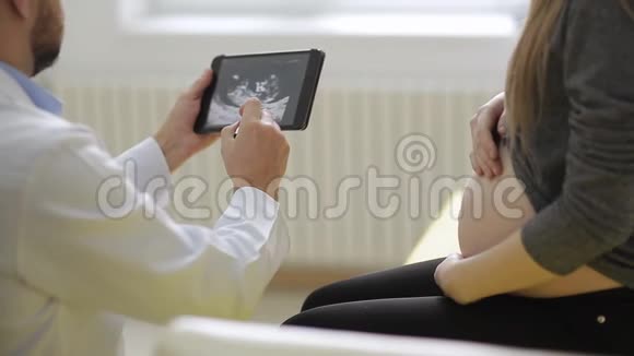穿着医用长袍的男医生给孕妇看了一张药片上的超声波照片视频的预览图
