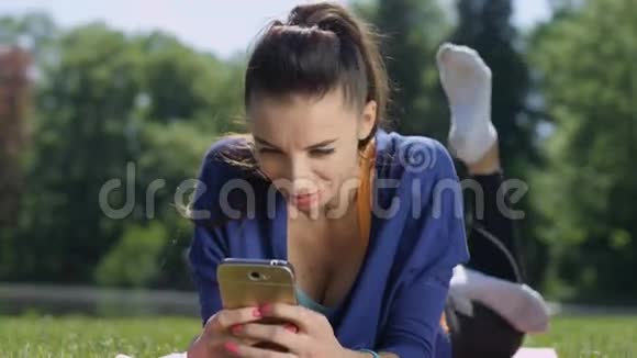 年轻迷人的女人躺在垫子上在阳光明媚的公园里用电话视频的预览图