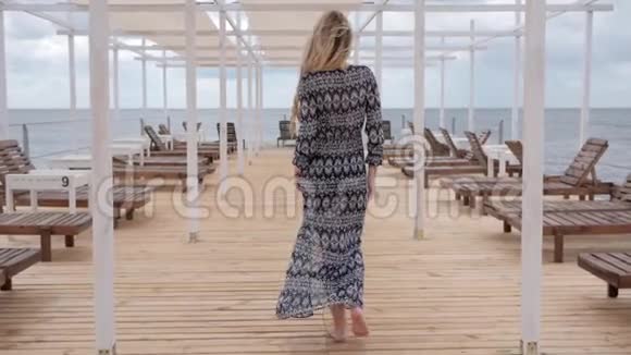 美丽的女人光着脚沿着码头走微风吹拂着海岸上女性的衣服放松着女孩视频的预览图