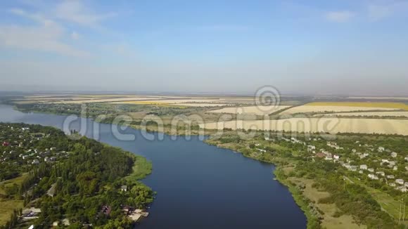空中俯瞰蓝色河流小村庄和河岸上的田野无人驾驶飞机拍摄乡村夏季景观视频的预览图
