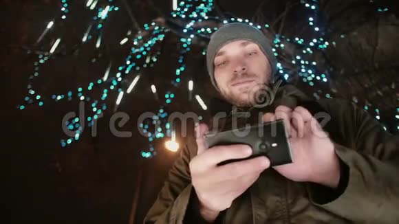 圣诞夜一个年轻的帅哥在一棵树下站着树上装饰着闪闪发光的灯视频的预览图