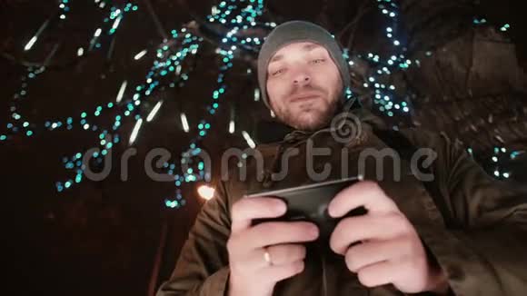 圣诞夜一个年轻的帅哥在一棵树下站着树上装饰着闪闪发光的灯视频的预览图