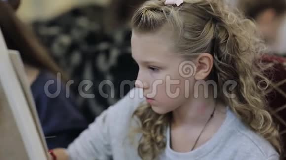 坐在画架上的漂亮少女在一所艺术学校画一幅画儿童专业艺术学校视频的预览图