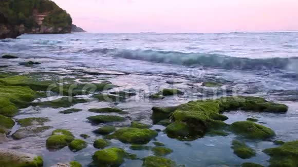日出时平静的海洋小波浪冲刷海滩上的岩石背景是山脉视频的预览图