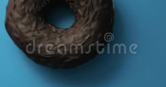 巧克力山核桃甜甜圈特写镜头旋转蓝色背景美味的甜面圈在盘子上旋转顶级视频的预览图
