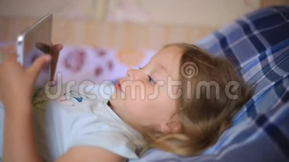 小白种人两岁的女孩躺在格子枕头上在平板电脑上看动画片现代技术视频的预览图