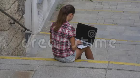 坐在楼梯上的女人在电脑键盘上打字视频的预览图