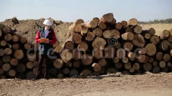 一个戴着白色头盔和红色夹克的建筑工人站在一堆原木附近视频的预览图