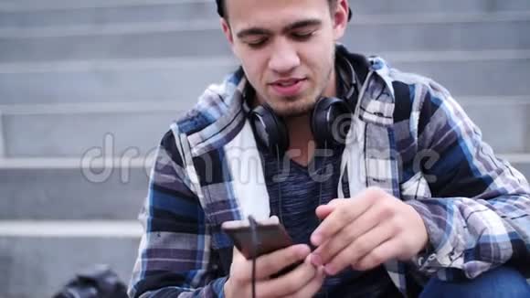 年轻人坐在户外的台阶上听智能手机上的音乐视频的预览图