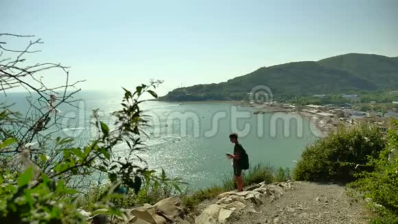 少年旅行者从塑料瓶里喝水男孩的旅程站在山岩悬崖海海湾上视频的预览图