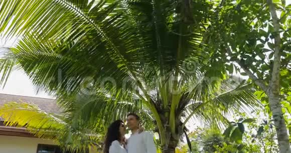 情侣漫步在别墅附近的热带花园中欢愉的男人和女人在度假时走出家门视频的预览图