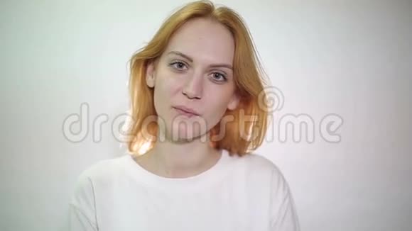 一个可爱的年轻白人女人在白色的背景上翻转她的红色头发视频的预览图