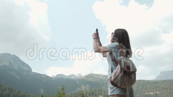 年轻女子用智能手机在山湖前拍照美丽的白种人女孩在一个女孩子中度过的时光视频的预览图