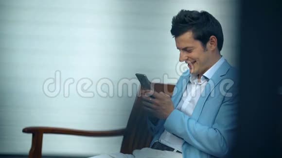 年轻的快乐男人坐在公园里用智能手机视频的预览图