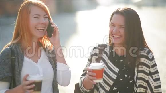 在阳光明媚的日子里女孩们带着电话和喝咖啡在城里走来走去视频的预览图