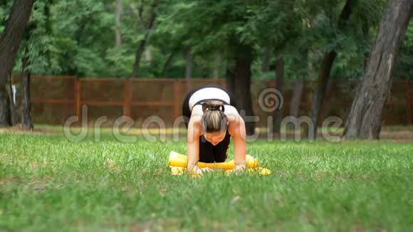 一位身穿运动服的年轻运动员女士在绿色草坪上的公园里躺在地毯上从事健身活动视频的预览图