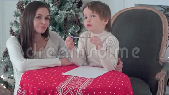年轻的母亲帮助她挣扎的儿子给圣诞老人写一封信视频的预览图