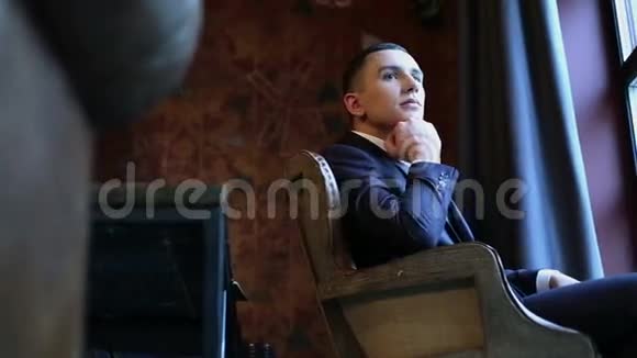 年轻迷人的男人坐在窗前的复古椅子上伸出手来托起下巴视频的预览图