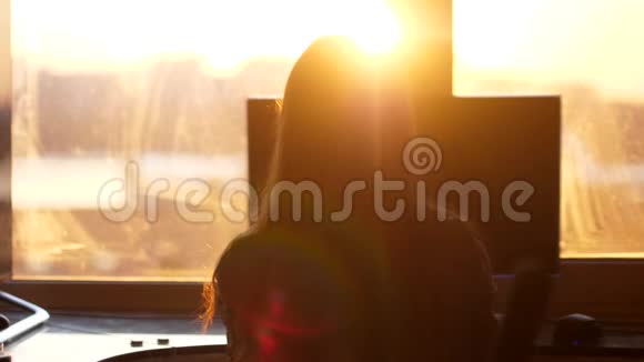 在美丽的夕阳下年轻的商务女性坐在窗边的一张桌子上在电脑上工作4k3840x2160视频的预览图