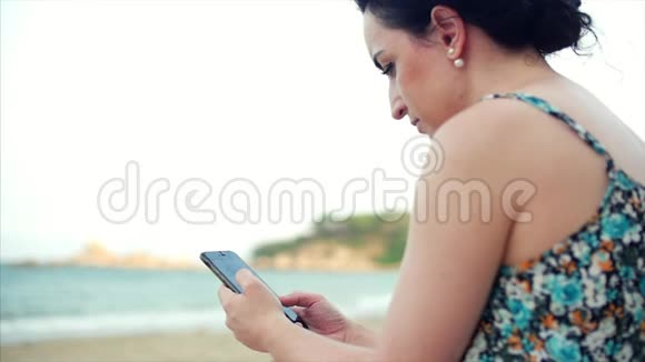 年轻的高加索女人在海边使用智能手机视频的预览图