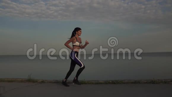 年轻女子沿着冲浪线轻轻地奔跑1女孩正在日落时慢跑视频的预览图