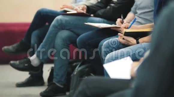 坐着听会议或演讲研讨会主课的人腿和手臂视频的预览图