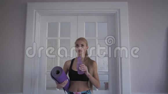 家庭健身从瓶子里喝干净的水年轻女子在训练靠近窗户视频的预览图