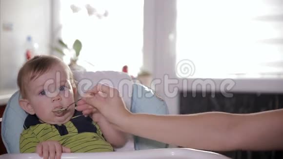可爱的微笑宝宝吃坐在宝宝的座位上在家里妈妈用勺子喂她可爱的一岁小孩视频的预览图