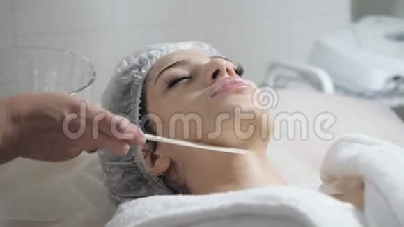 用刮刀泡沫从面部取出年轻漂亮的女人在美容院接受治疗面部清洁泡沫视频的预览图