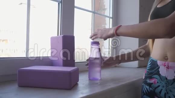 家庭健身从瓶子里喝干净的水年轻女子在训练靠近窗户视频的预览图