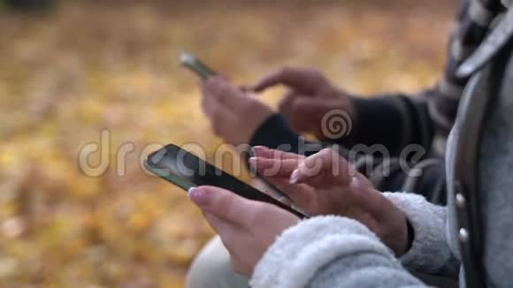 年轻的男女在秋天的公园里坐在长凳上用电话注意女孩的双手视频的预览图