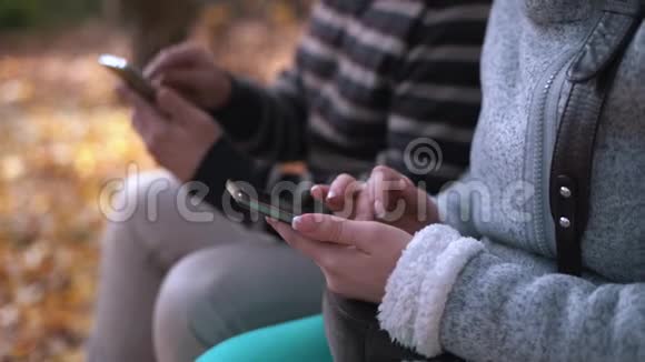 年轻的男女在秋天的公园里坐在长凳上用电话注意女孩的双手视频的预览图