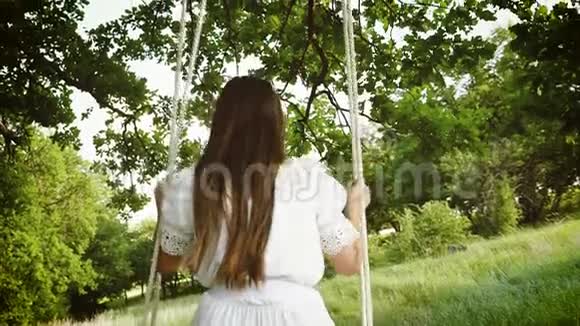 长发女孩在夏天公园的秋千上荡秋千慢动作视频的预览图