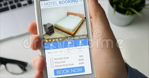 男人用他的智能手机和在线预订手机应用程序坐在他的办公桌上预订酒店西装视频的预览图