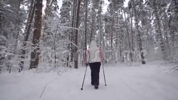 在树林里的雪道上行走的一位老年妇女的后景现代形式的运动视频的预览图