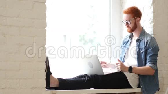 在笔记本电脑上在线视频聊天坐在窗口的休闲男子视频的预览图