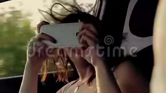 夕阳下一个年轻漂亮的女孩坐在一辆带电话的车里视频的预览图