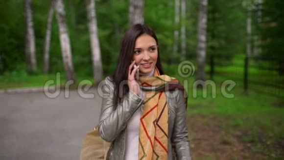 美丽的年轻女子带着迷人的微笑在她的手机上说话夏天在户外慢动作视频的预览图
