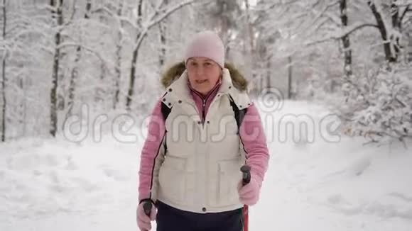 穿着漂亮运动服装的老年妇女在冬季森林的雪道上行走现代养恤金视频的预览图