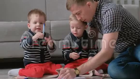 家里的爸爸和两个双胞胎兄弟一起画记号笔把毛笔放在地板上视频的预览图