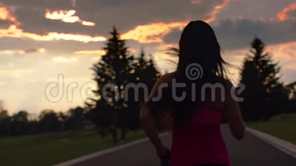 日落时分在公园里奔跑的女人晚上在公园里跑女人的后景视频的预览图
