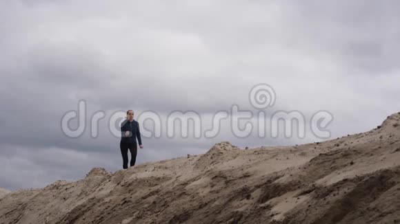 身材苗条的妇女慢跑者在沙漠中跑步黑暗风暴云在背景视频的预览图