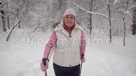 穿着漂亮运动服装的老年妇女在冬季森林的雪道上行走现代养恤金视频的预览图