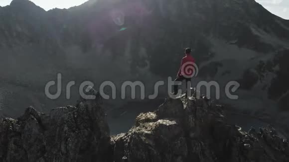 一个留着胡子戴着帽子戴着墨镜的年轻嬉皮士正站在高高的山上的岩石山脊上视频的预览图
