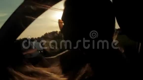 风吹过女孩的剪影和头发在车里日落视频的预览图