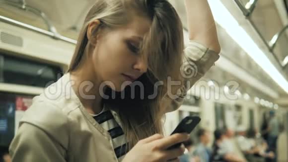地铁列车上一位微笑可爱的女孩在手机上打字留言的肖像一位金发女学生与视频的预览图