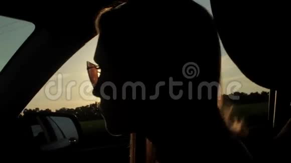 风吹过女孩的剪影和头发在车里日落视频的预览图