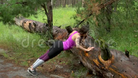森林里的健身女孩在老树上练习俯卧撑练习视频的预览图