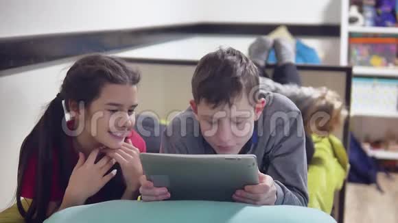 男孩和女孩躺在床上的平板电脑上在户外玩耍男孩和女孩青少年社交媒体互联网上的平板电脑视频的预览图