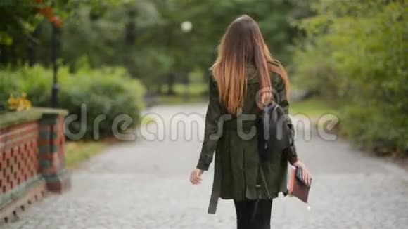 一个快乐的年轻女子走在城市公园附近的人行道上学生女孩拿着笔记本温暖的秋日视频的预览图